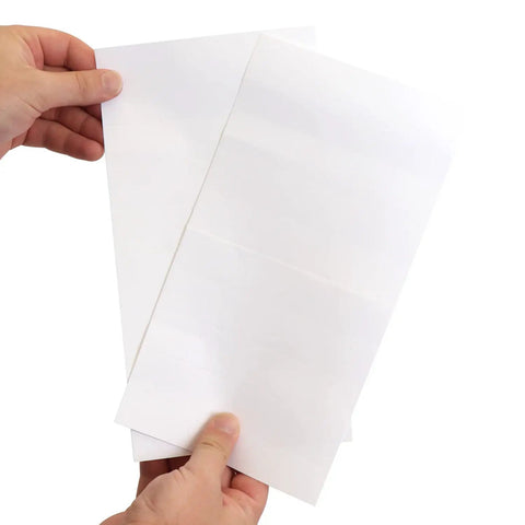 Hands holding two white sheets of paper, representing uses for Slick Clear Plastic Shelf Clip Label Holders Fits One Inch Thick Racks No Sweat Installation Perfect For Warehouse Storage And Retail Inventory Management Pack Of Ten.