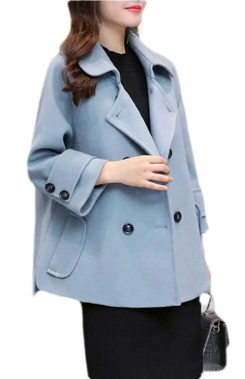 Light blue women's coat with wide collar and double-breasted buttons, worn over black dress with handbag.