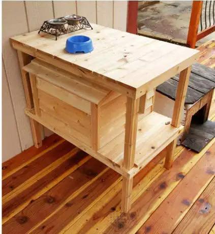 Chillin In Style With Your Favorite Feline Pal This Elevated Cedar Cat House Packs Serious Insulation And A Raised Two Level Loft To Keep Outdoor Pets Cozy Dry And Protected, showing a wooden elevated cat house with food bowls.