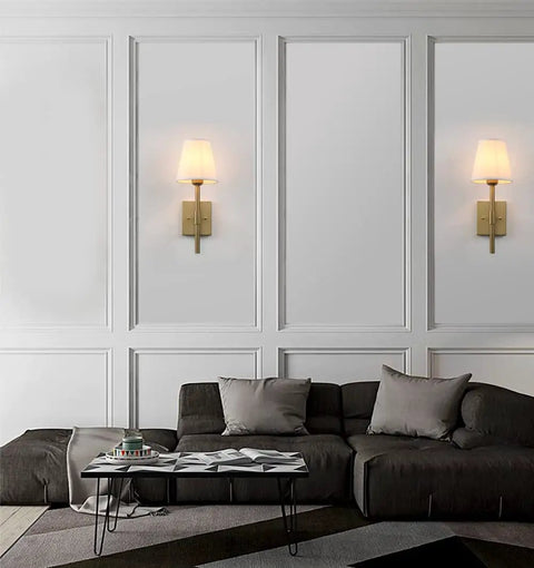 Set Of 2 Hardwired Wall Sconces With White Fabric Shade, Brass Finish Bases, illuminating a cozy living room setting.