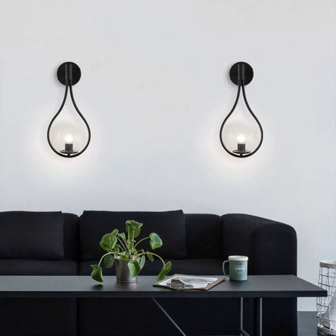Industrial Vintage Matte Black Globe Wall Sconce Set of 2 With Clear Hand Blown Glass Shades above a black sofa in a living room.