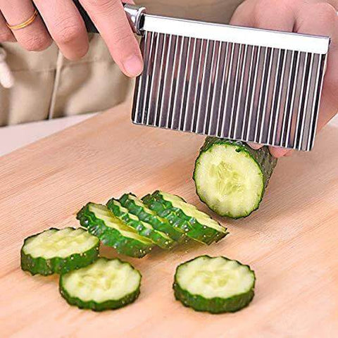 Kitchen vegetable slicer with steel wavy blade slicing cucumber rounds on a cutting board