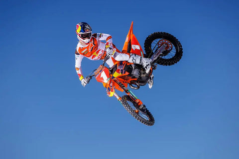 Motocross rider in mid-air jump on orange bike against blue sky background