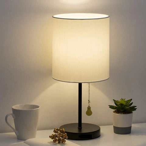 Table lamp with decorative shade on, showing the hanging pull chain with ball connector against a soft illuminated background.