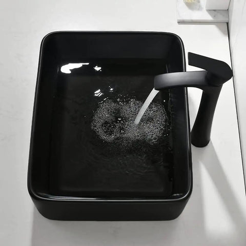 Black rectangular vessel sink with modern faucet, shown with running water and sleek countertop, above-counter installation.