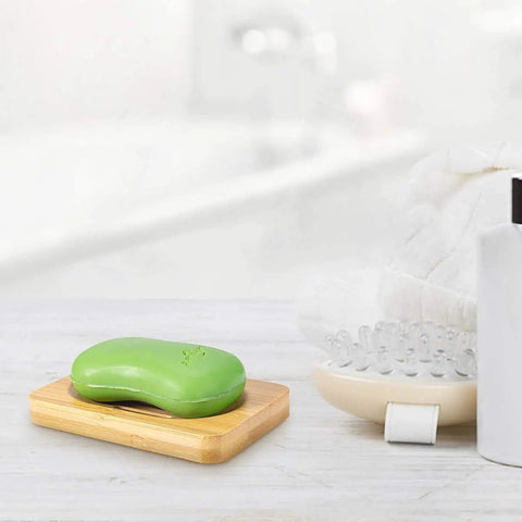 Green soap on bamboo dish with bath accessories, part of Bamboo Shower Bench With Foot Stool, 2 Tier Wood Spa Bath Organizer Seat.