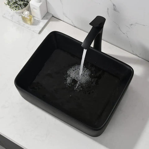 Black rectangular vessel sink with running water on marble counter