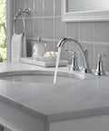 Woodhurst Chrome 3 Hole 8 Inch Widespread Bathroom Faucet with flowing water on a marble vanity, visible drain in elegant setup.