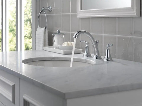 Woodhurst Chrome 3 Hole 8 Inch Widespread Bathroom Faucet with flowing water on a marble vanity, visible drain in elegant setup.