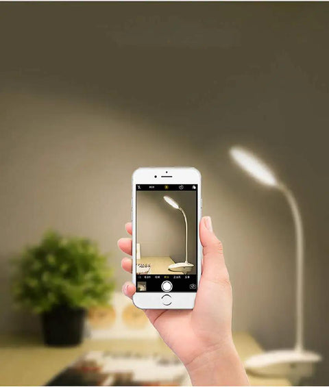Hand holding phone with Clip On Bedside Reading Lamp With USB Rechargeable Battery, 18 LED Eye Friendly Light in the background
