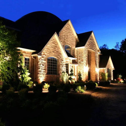 JUDYSSY Outdoor Solar Flood Lights illuminating a garden and house at night with warm light against a dark sky.
