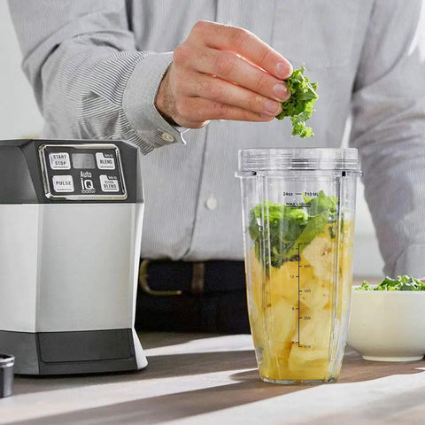 Person adding ingredients to 24oz Blender Cups With Sip And Seal Lids Replacement Parts For Auto IQ Series Blenders