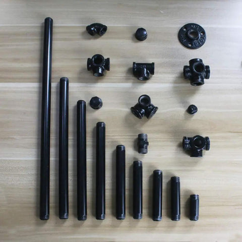 Assorted black metal pipes and fittings on wooden surface for DIY enthusiasts building sick industrial shelving and home decor projects.