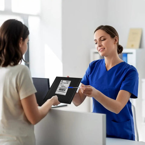 Person handing over Six By Ten Inch Bubble Mailers 100 Pack Black Padded Envelopes Waterproof Self Seal Opaque at a counter.