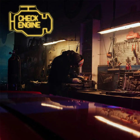 Mechanic working in dimly lit garage with a "Check Engine" neon sign on the wall.