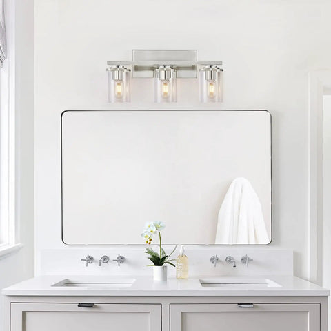 Three Light Brushed Nickel Bathroom Vanity Light Fixture With Clear Glass Shade Over Mirror in modern bathroom setting.