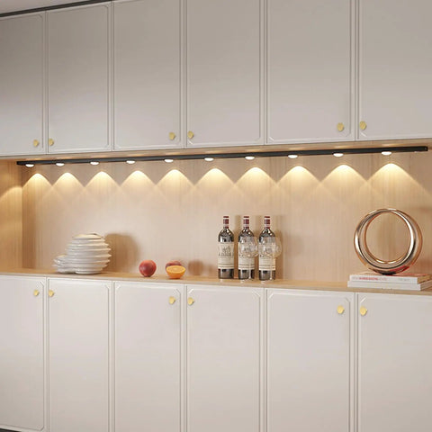 White kitchen cabinets with gold brass drawer knobs under countertop lighting, featuring smooth finish and modern decor items.