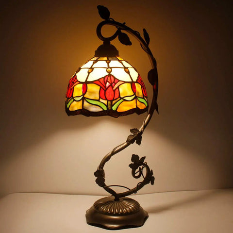Red Tiffany Style Stained Glass Tulip Table Lamp With Bronze Metal Leaf Base lit up in a dark room