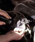 Person using Stinger 425 Lumen LED Rechargeable Handheld Flashlight With 12V DC Charger Tough Aluminum Body Non Slip Grip IPX4 Water Resistant 1 Meter Drop Tested High Med Low Strobe Long Runtime On Low to illuminate car engine