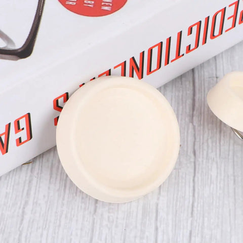 Close-up of a 4pcs White Rubber Bathtub Stopper with Hanging Ring for Sink Drains on textured surface next to a book.