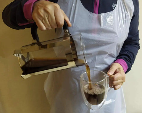 Person pouring coffee wearing Poly Disposable Apron Individually Wrapped 40 Count Waterproof PE From Neck To Knee Full Size Bib Type