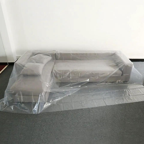 Two Pack 4 Mil Plastic Drop Cloths 9 By 12 Feet Waterproof Heavy Duty Clear Tarp covering a grey sofa in a living room