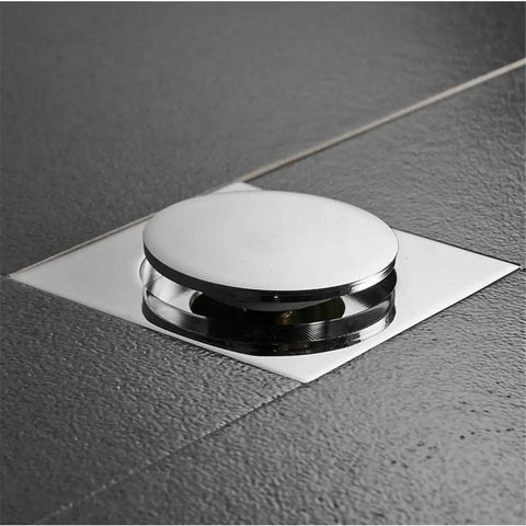 Pop Up Foot Floor Drain Push Down Bathtub Plug Built Tough Brass Chrome Finish with a square tile cover on grey surface.
