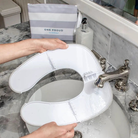 Foldable Travel Potty Seat For Toddlers being cleaned at a sink, showing slim design and lightweight material.