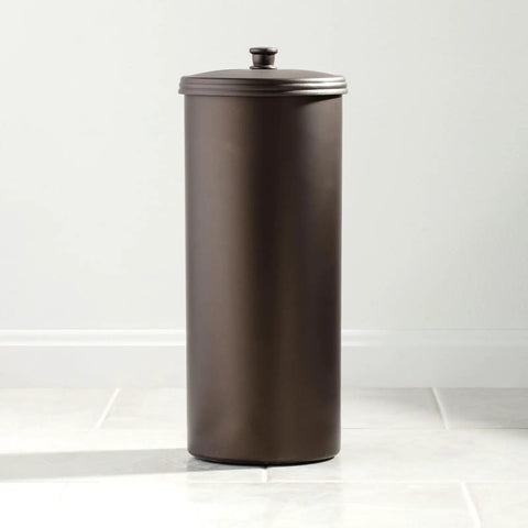 Bronze metal standing toilet roll holder on tiled bathroom floor with lid closed.
