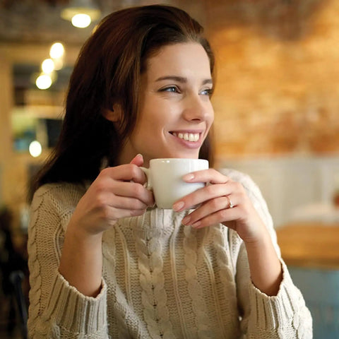Woman smiling while holding a coffee cup, enjoying a smooth brew made with 24 Pack Replacement Charcoal Water Filter Discs.