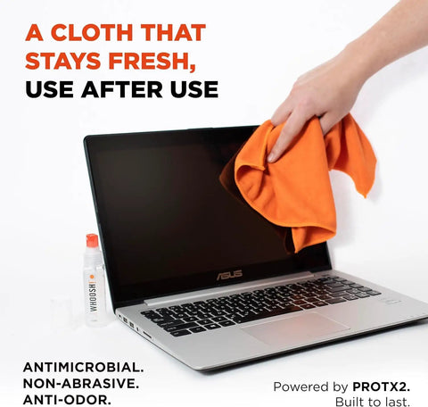 Person cleaning laptop screen with orange cloth from refillable screen cleaner kit, bottle visible beside laptop.