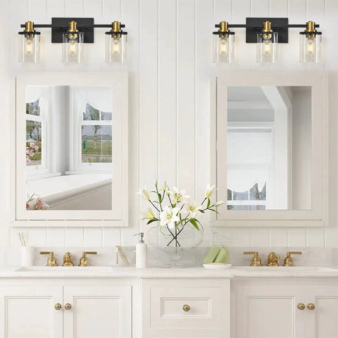 Three Light Black And Gold Bathroom Vanity Light Fixtures Over Mirror With Clear Glass Shade shown in modern bathroom setting