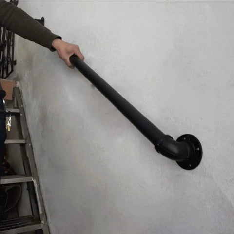 Heavy Duty Rustic Pipe Railing And Wrought Iron Stair Banister For Indoor Porches And Outdoor Decks With Super Tough Wall Braces For Legit Safety And Next Level Style Flex hand gripping black pipe railing on a wall.