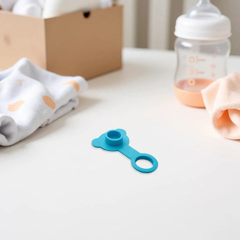 Blue Silicone Bathtub Drain Plug Stopper for Easy Removal on a table with baby clothing and bottle.