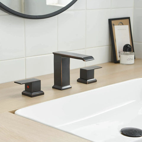 Oil Rubbed Bronze Widespread Bathroom Faucet With 8 Inch 3-Hole Mount 2-Handle Waterfall Vanity Lavatory Tap Modern Sink Fixture With Pop Up Drain And Overflow For RV Or Home installed on a light wood vanity.