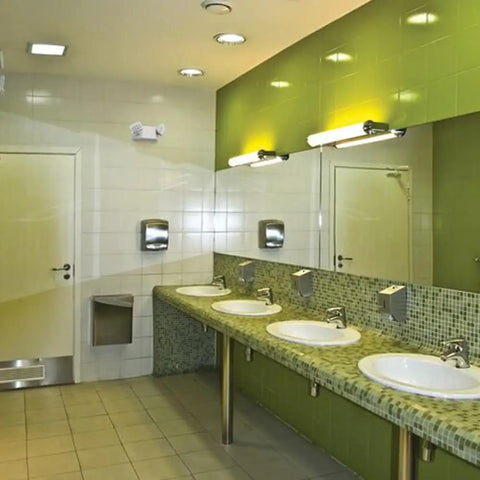 Basics LED Emergency Light With Dual Adjustable Lamp Heads For Wall Mount in a restroom, on white tile wall above sinks.