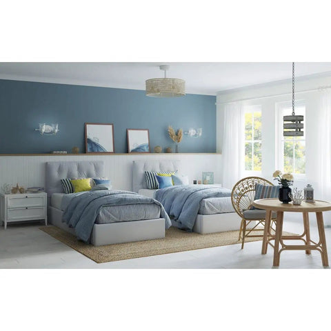 Calm coastal bedroom with twin beds, light blue walls, and a round rattan dining table near window. Pendant light overhead.
