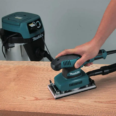 Hand using Beast Of A Sheet Finishing Sander One Third Inch Orbit, 1.7 Amp, Teal Finish With Ergonomic Rubberized Grip on wood surface