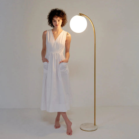 Woman standing next to Luna Drop 75 Inch Antique Brass Floor Lamp With Frosted White Glass Globe Shade, stylish room decor.