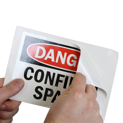 Danger Confined Space OSHA Sticker Labels 5x7 Inch 5 Mil Laminated Polyester With SuperStick Adhesive being peeled, close-up view.
