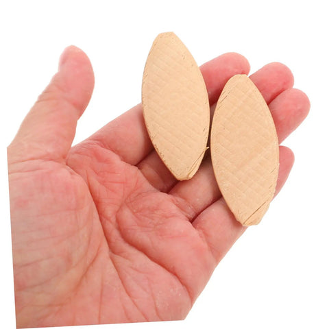Hand holding two light yellow wood joiner biscuits, part of 100 pcs set for woodworking and carpentry projects, offering quick strong connections.