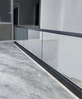 Heavy Duty Glass Railing System For Deck And Balcony Featuring Rock Solid Spigot Clamps with matte black aluminum posts on a modern floor.