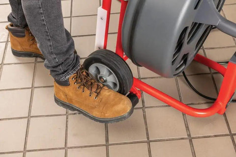 Person's foot operating the wheel of the Heavy Workhorse 115 Volt Drain Cleaning Machine With Auto Feed Cable Control.