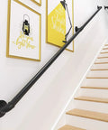 Heavy Duty Rustic Pipe Railing And Wrought Iron Stair Banister For Indoor Porches And Outdoor Decks With Super Tough Wall Braces For Legit Safety And Next Level Style Flex installed on white wall next to wooden stairs.