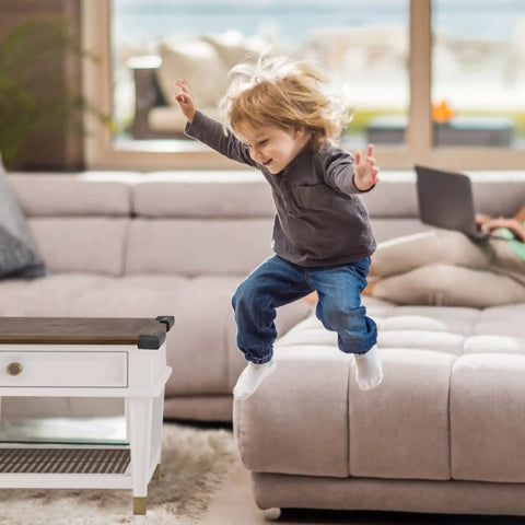 Child jumping on sofa with furniture edge protected by 12 Pack Soft Corner Protectors For Baby Proofing Edge Guards With Pre-Taped Rubber Foam