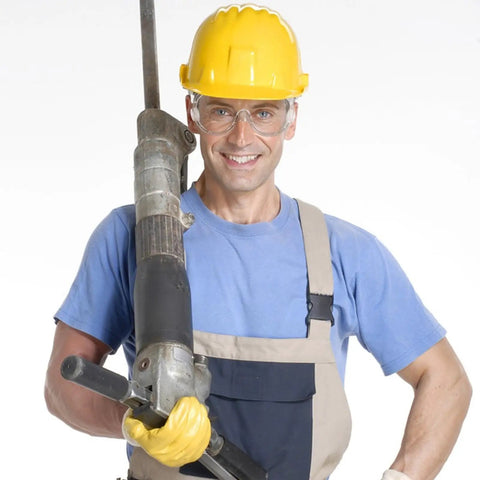 Worker wearing Badass Protective Safety Goggles With Anti Fog Clarity and Scratch Resistant Lenses, yellow hard hat, and gloves, holding a tool.