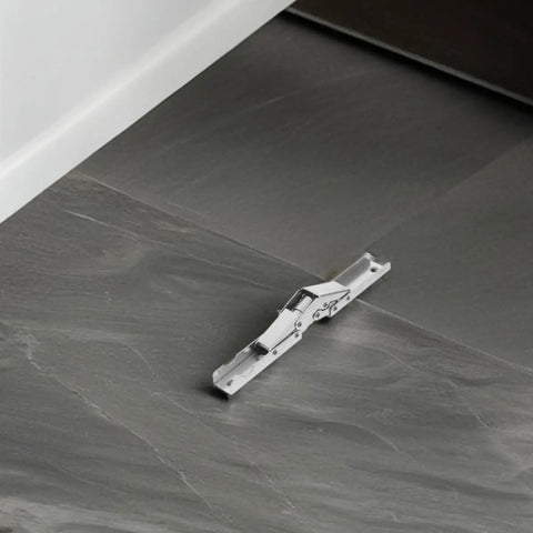 Close-up of space saving corner cabinet hinges with short arm wide angle design in cold rolled steel on gray tile floor.