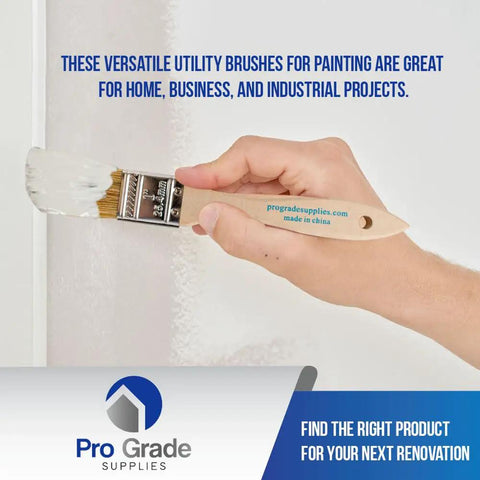 Hand holding Chip Paint Brushes Pack 24 Count 1 Inch Wide With White Bristles And Light Brown Square Trim Handles Do It All For Painting Stains Varnish Acrylic Or Gesso Great For Home Projects And Light Industrial Use against white wall