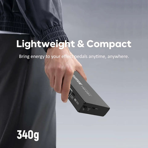 Person holding a Rechargeable Guitar Pedal Power Supply with 12800mAh High-Current Battery, Model PB-051, compact design