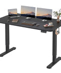 55 By 24 Inch Electric Height Adjustable Standing Desk For Home Office With Memory Preset And T Shaped Metal Bracket Big Sit Stand Computer Desk Black, shown with laptops and accessories on the black desktop.